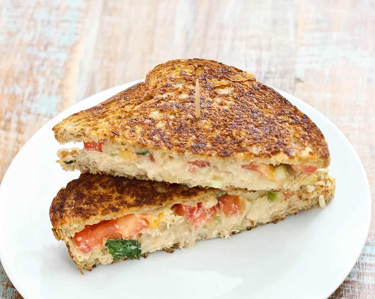 chicken salad melt sandwich halves stacked on top of each other and secured with a toothpick on a white plate.