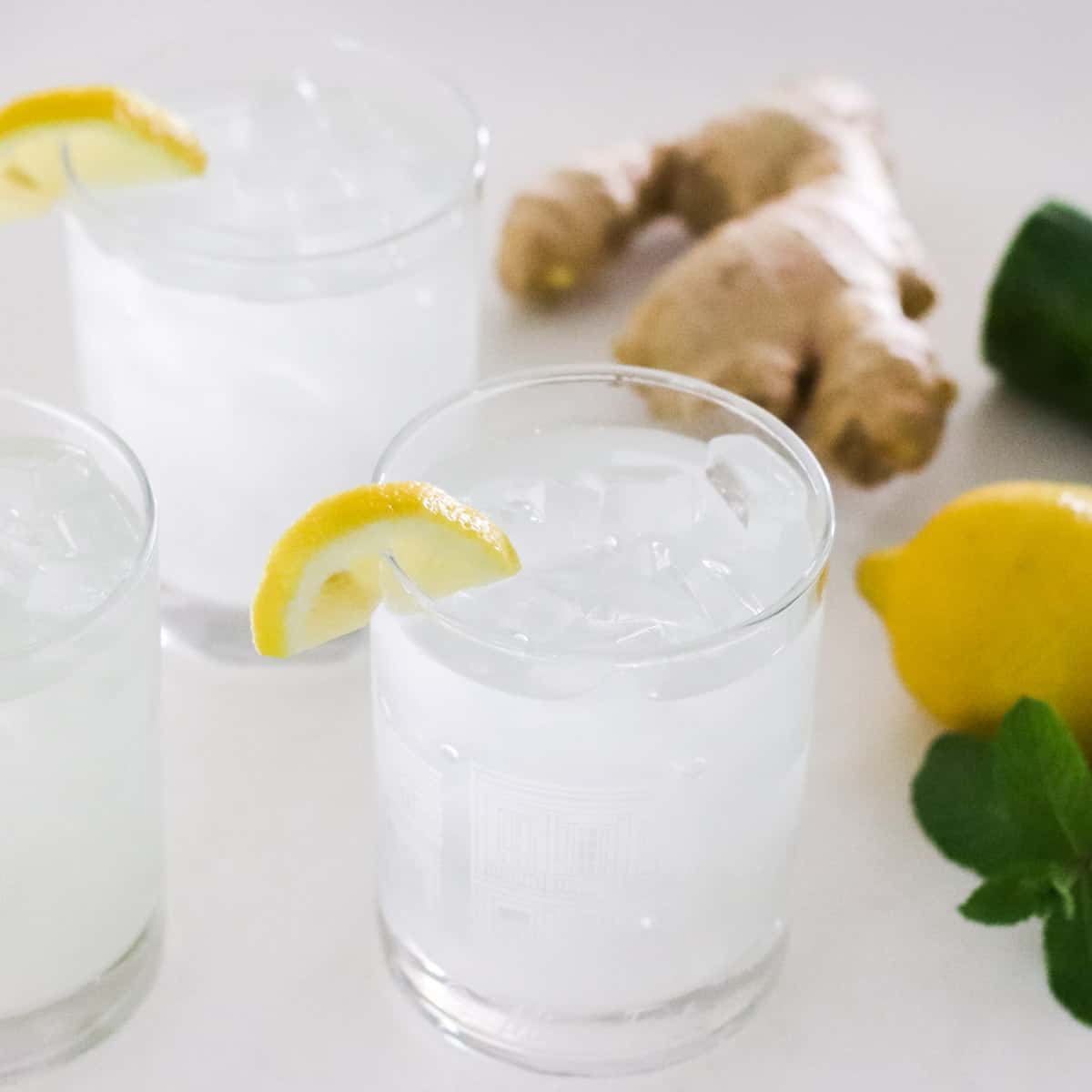 glasses with ginger lemon and cucumber water next to fresh mint, lemon, ginger, and cucumber.