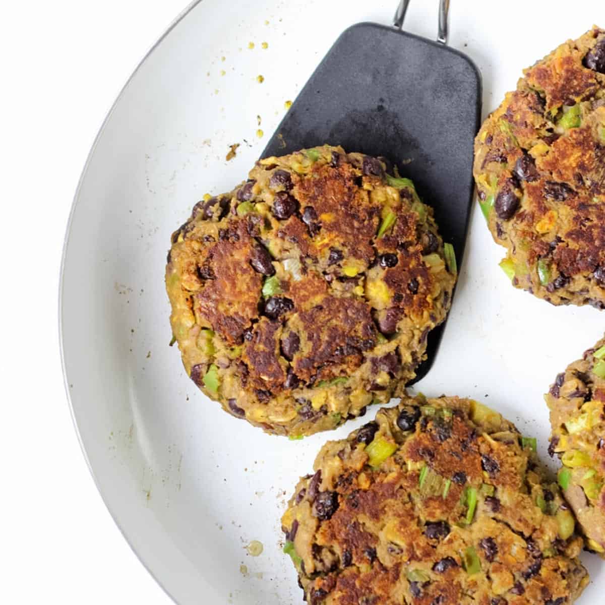 white skillet with avocado black bean burgers and a black spatula flipping on of the burgers.