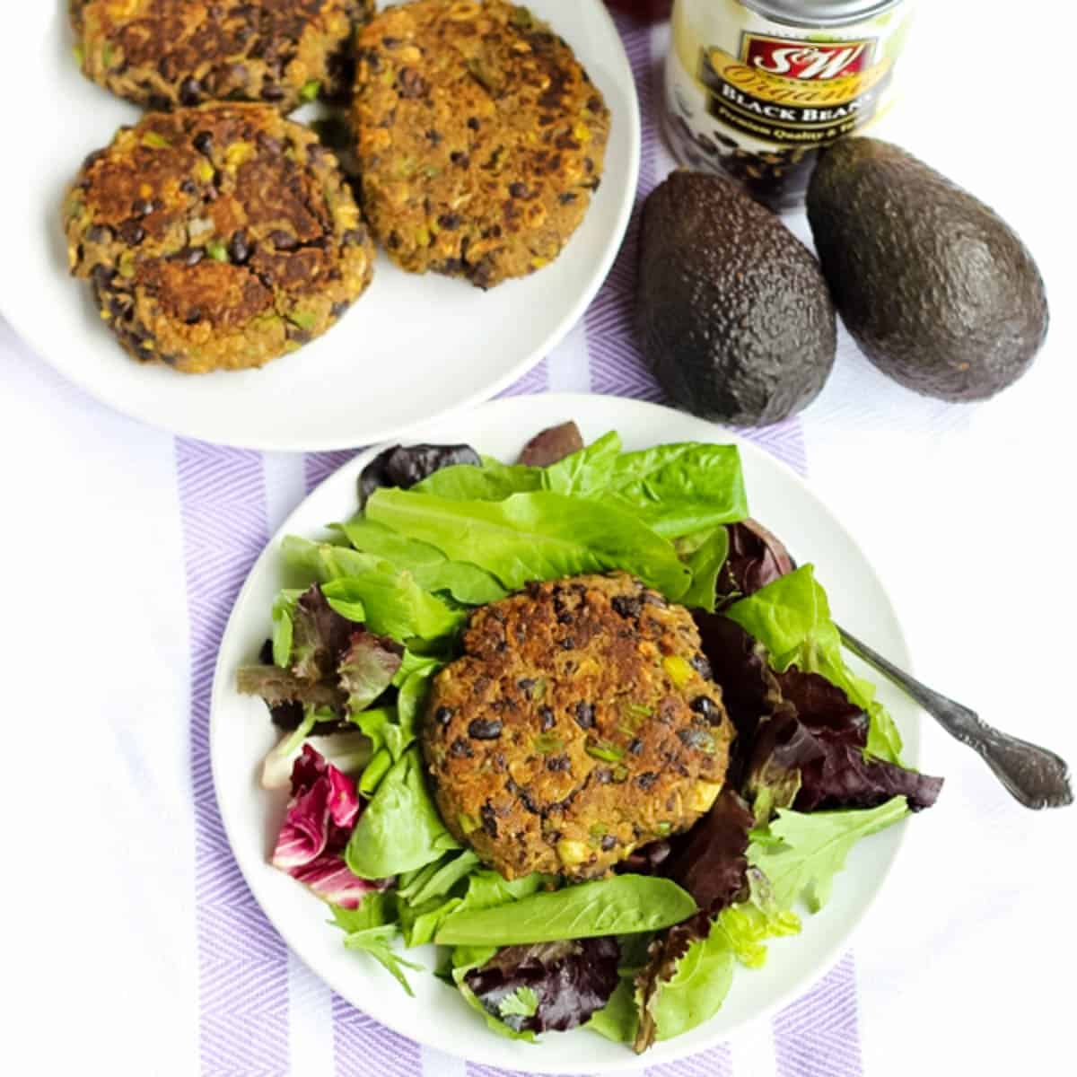 white plates with avocado black bean burgers and a bed of lettuce with one black bean burger on top all on a white and purple striped towel.