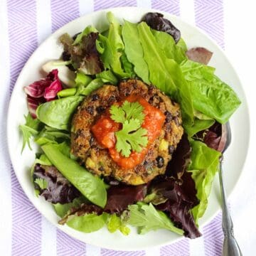 white and purple towel with white plate full of lettuce topped with veggie burger with avocado, topped with salsa and cilantro.