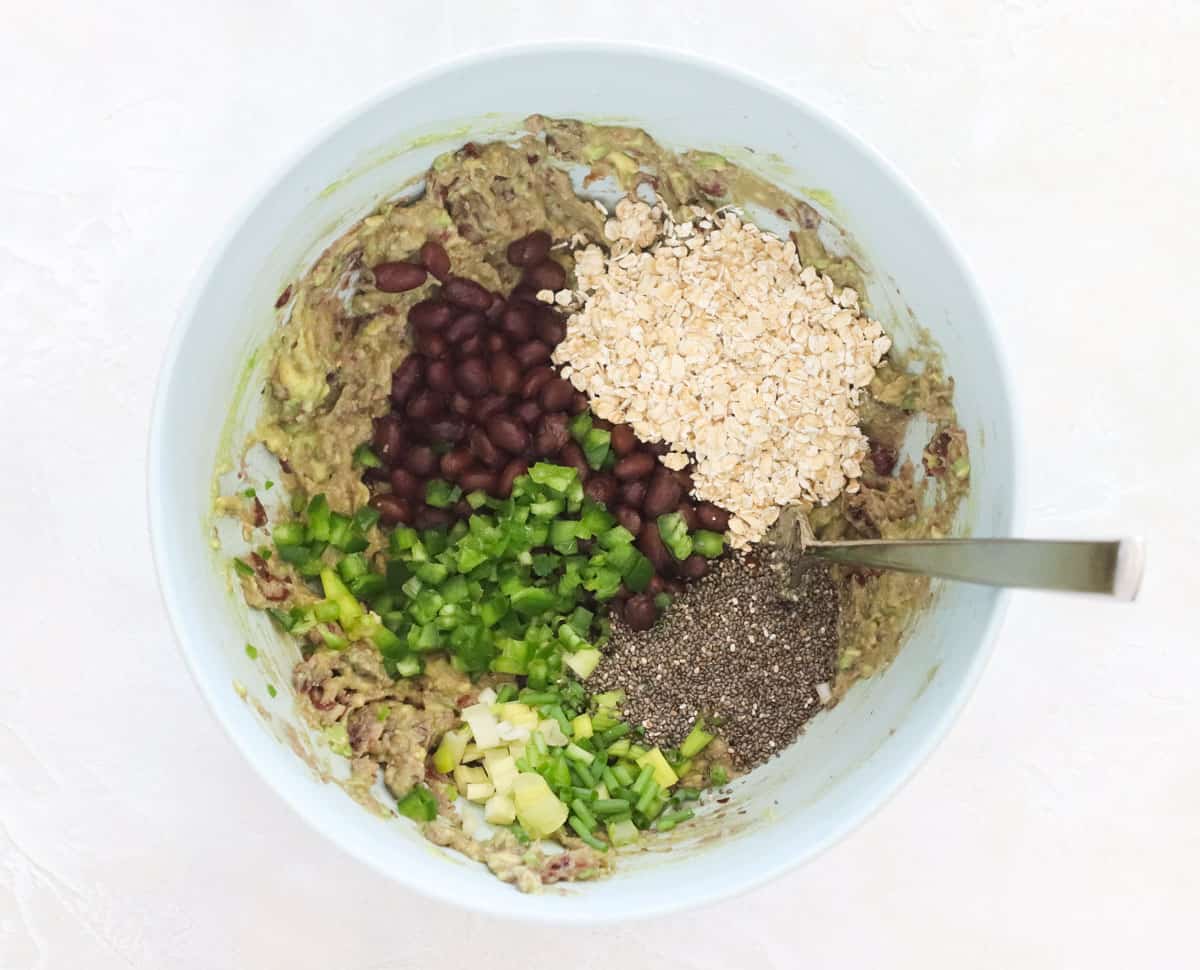blue bowl with mashed avocado and black beans with chia seeds, jalapeno, oats, and green onions added to it.
