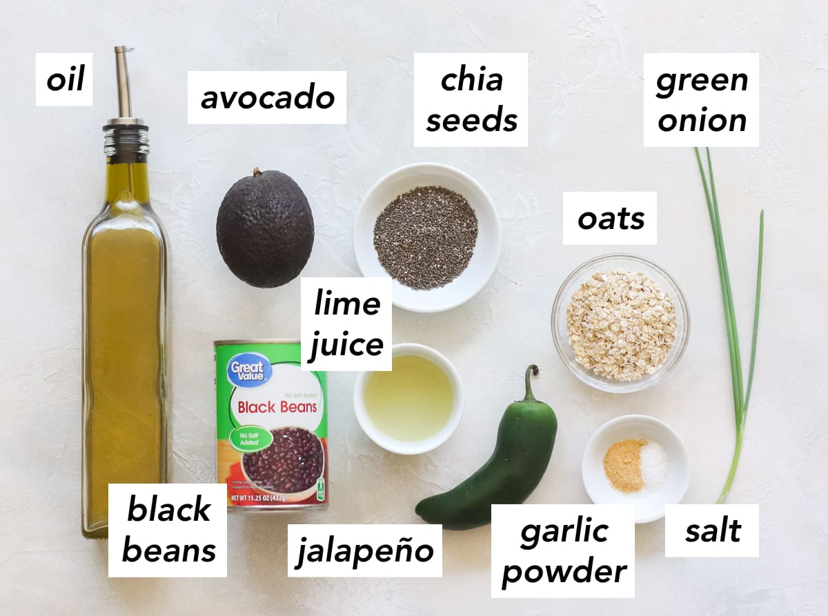 bottle of olive oil, avocado, can of black beans, bowl of lime juice, bowl of chia seeds, fresh jalapeno, bowl with garlic powder and salt, bowl of oats, and a fresh green onion.
