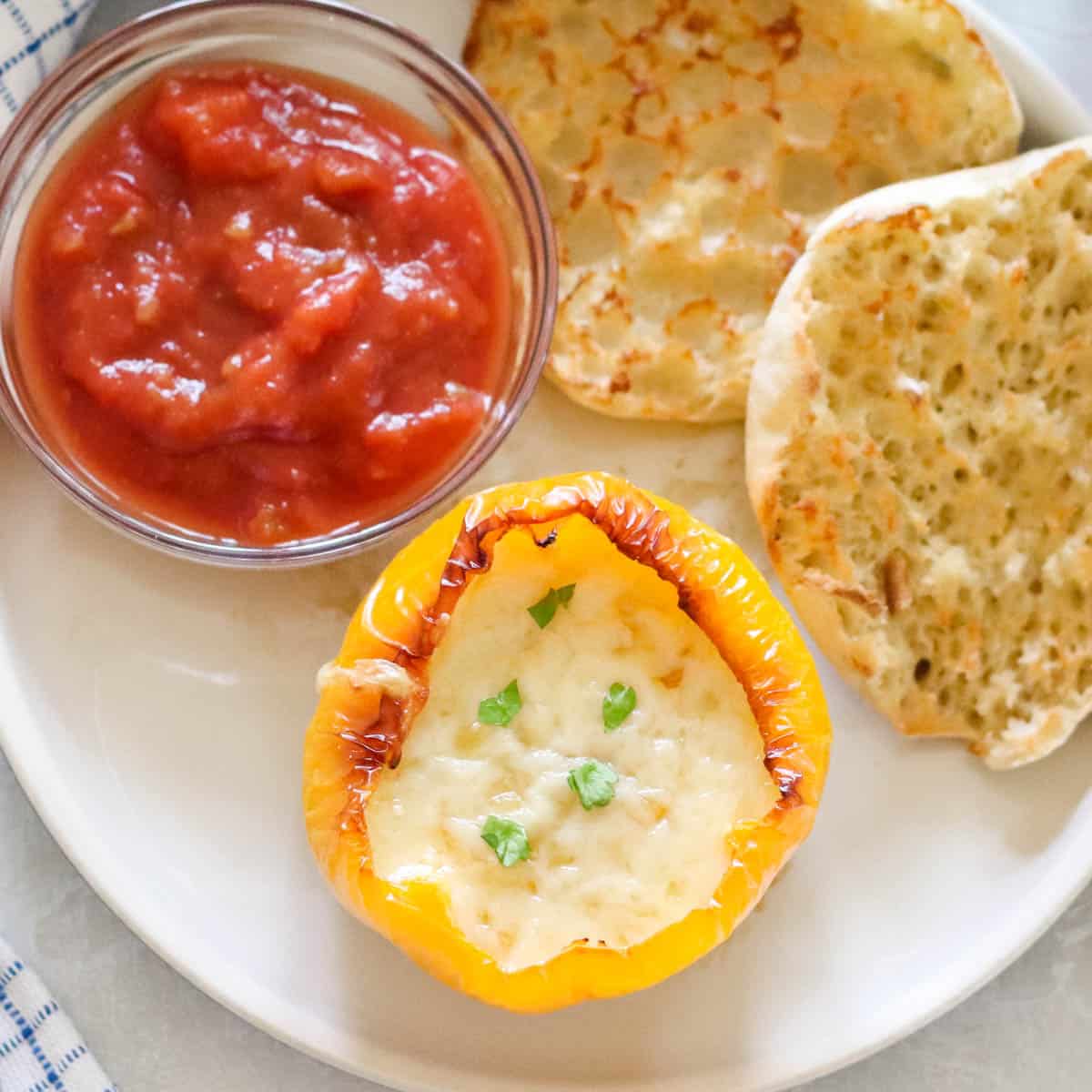 plate with a bowl of salsa, english muffin, and yellow breakfast stuffed pepper.