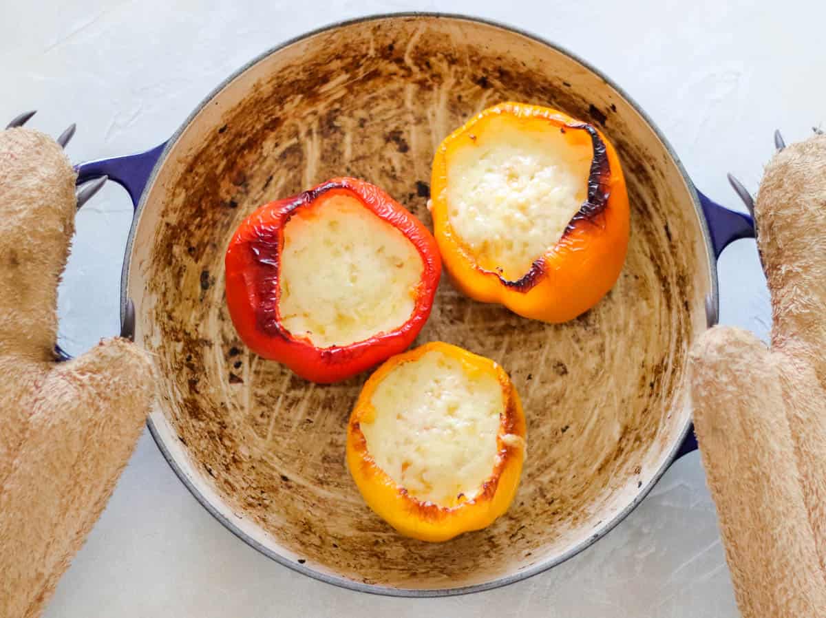 bear oven mitts holding a pot with baked stuffed bell peppers with eggs and cheese.