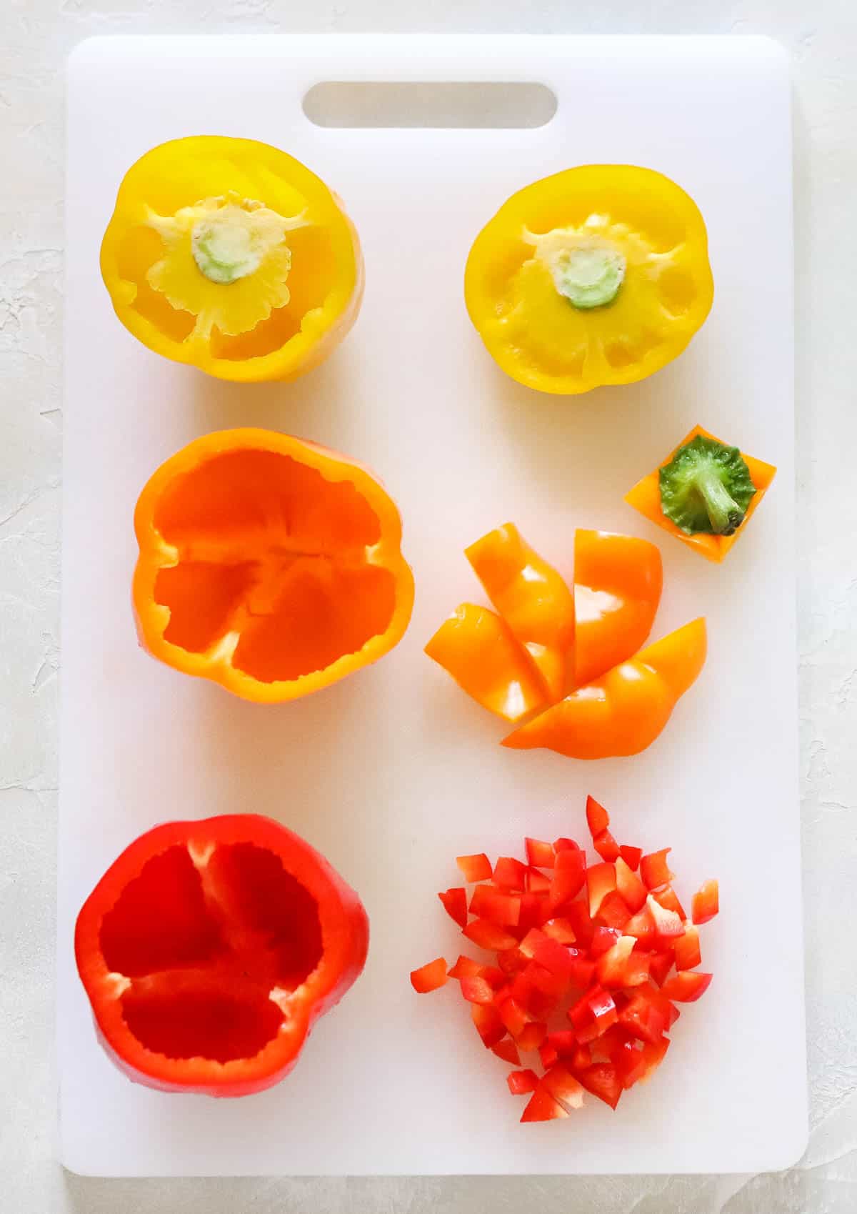 white cutting board with yellow, orange, and red bell peppers with their tops removed and chopped.