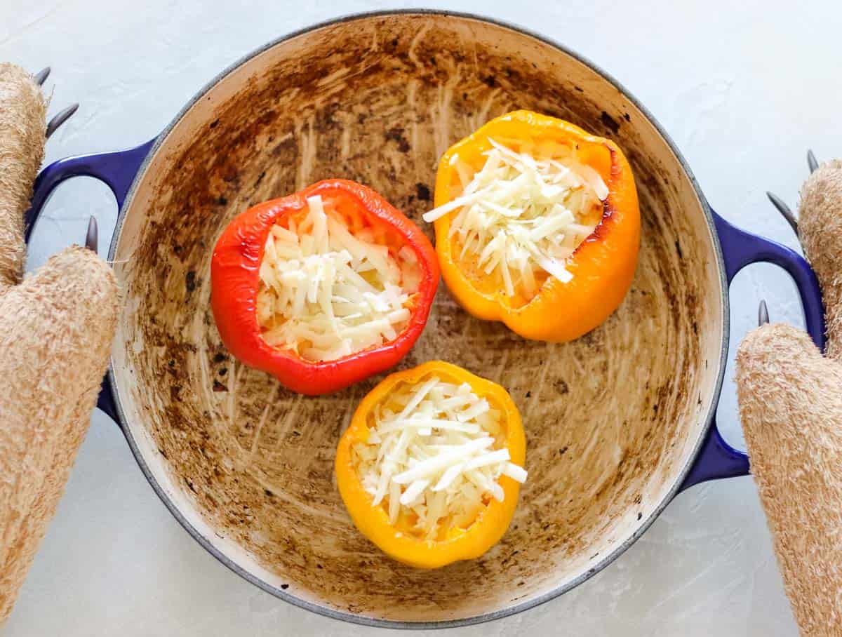 bear paw oven mitts holding a blue pot with red, yellow, and orange bell peppers filled with eggs and cheese.