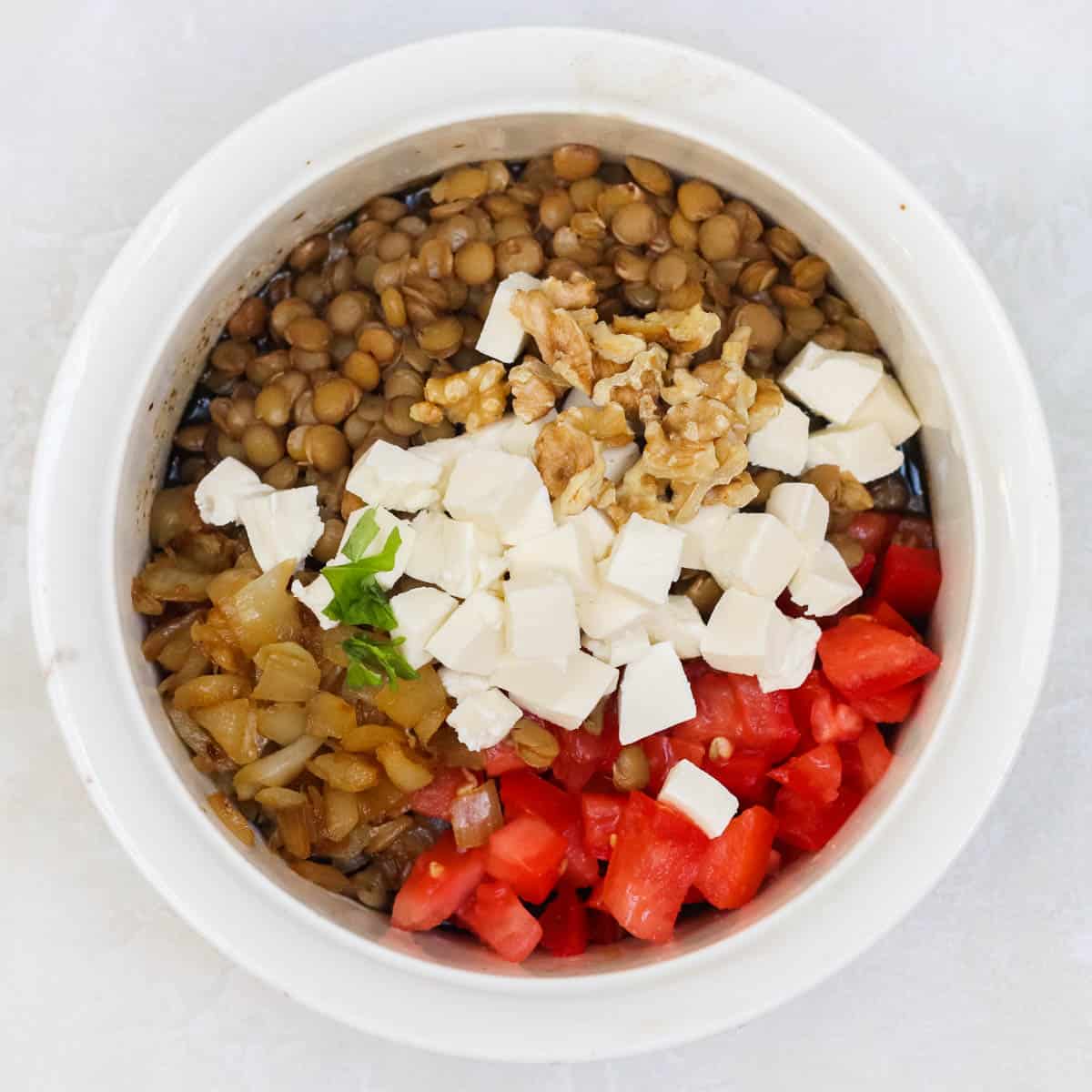 white bowl with cooked lentils and onions, fresh diced tomatoes, diced mozzarella, fresh basil, and chopped walnuts.