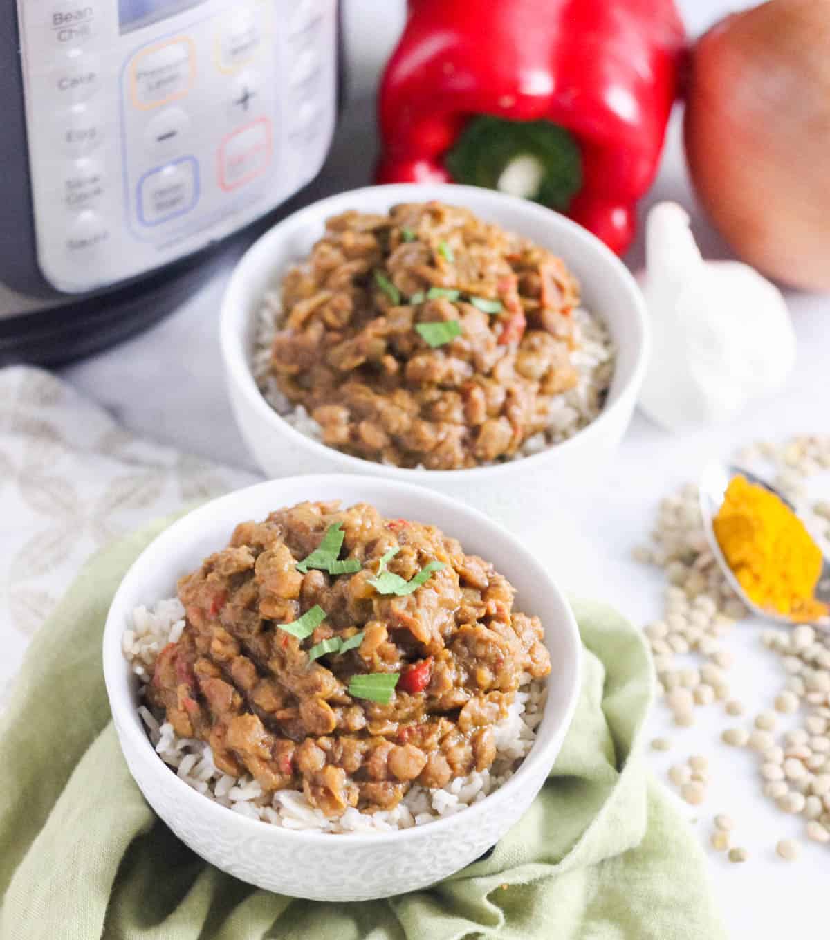 green napkin, white bowls with lentil curry over rice, scattered lentils, spoon of turmeric, red bell pepper, garlic, onion, and an Instant Pot.