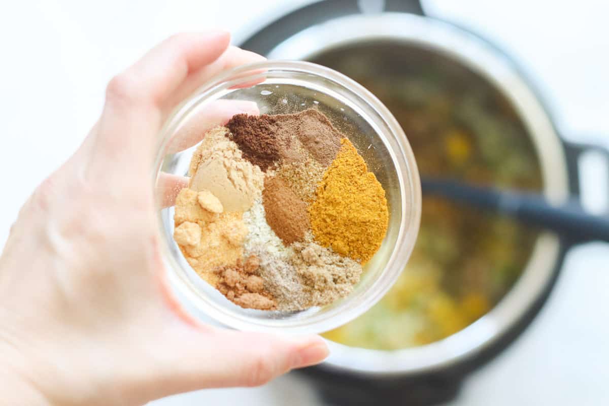 hand holding a bowl of spices over an Instant Pot.