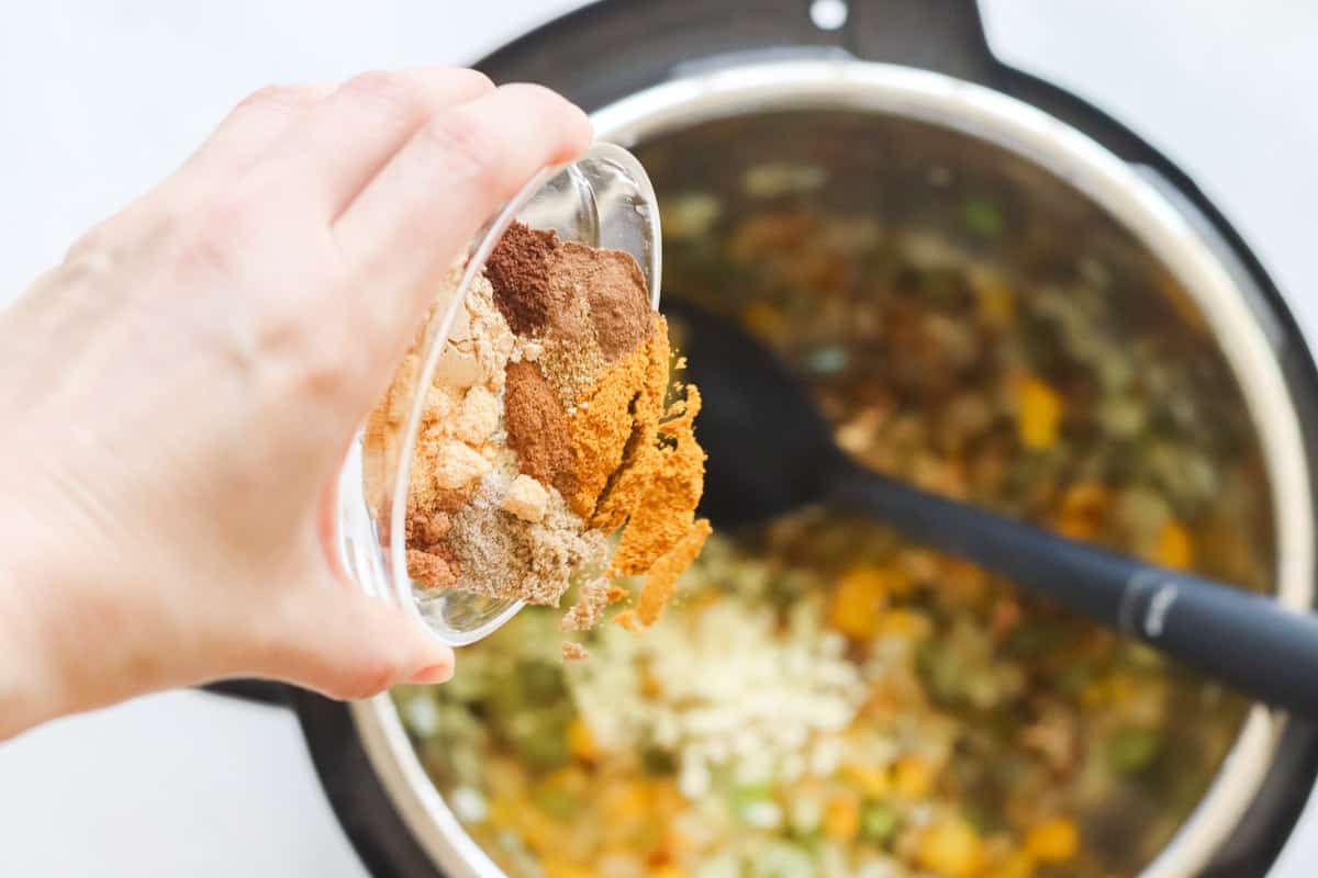 hand pouring a bowl of spices into a pressure cooker with veggies.