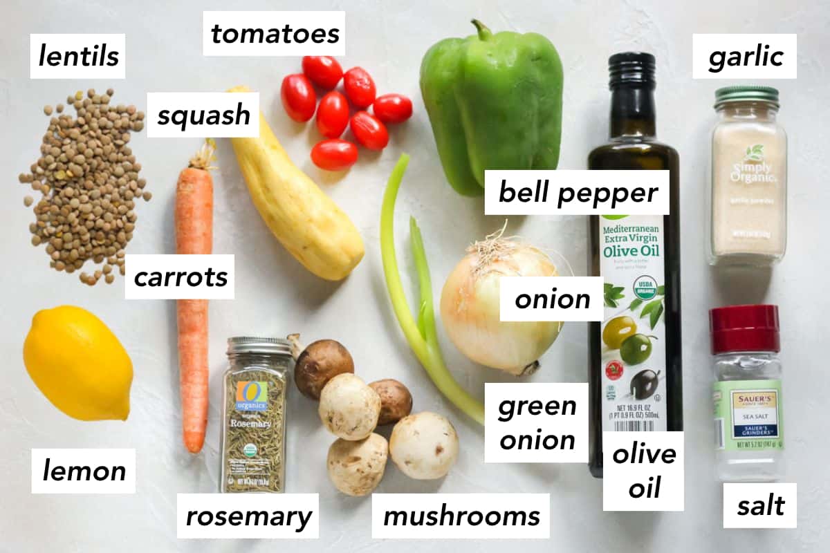 scattered lentils, lemon, carrot, jar of dried rosemary, mushrooms, green onion, yellow onion, bottle of olive oil, salt shaker, jar of garlic powder, green bell pepper, cherry tomatoes, and yellow squash.