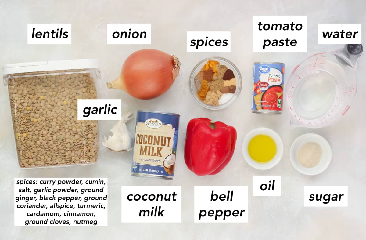 container of lentils, head of garlic, yellow onion, bowl of spices, can of coconut milk, red bell pepper, bowl of olive oil, bowl of sugar, measuring cup of water, can of tomato paste on a counter with text overlay describing each ingredient.