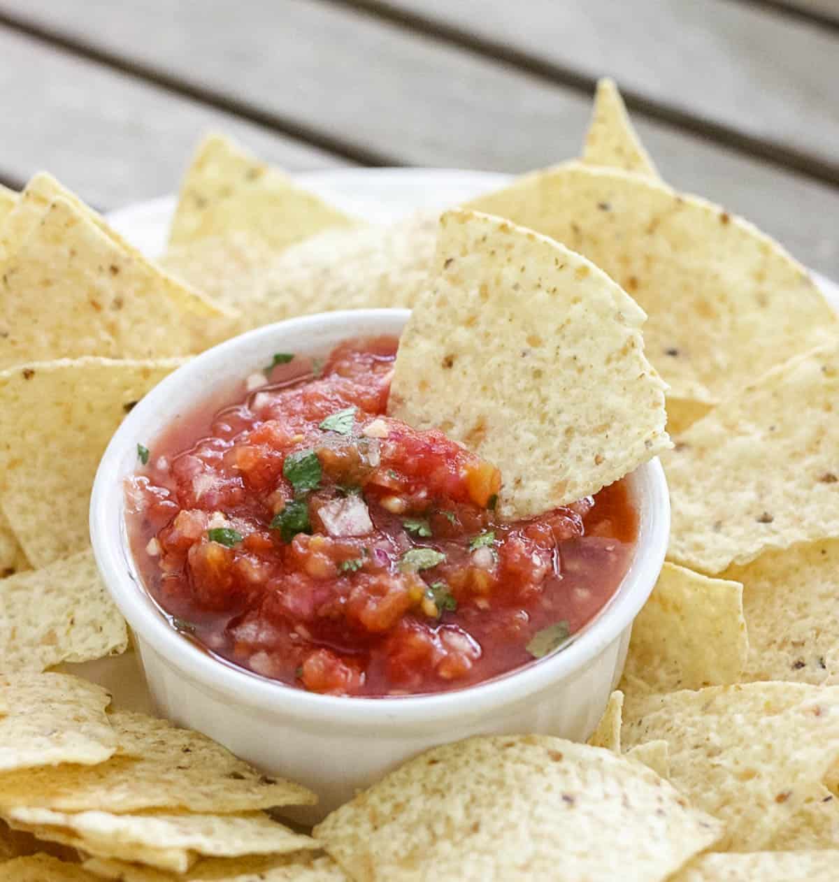 plate of chips with bowl of salsa and a chip sitting in salsa with canned tomatoes.