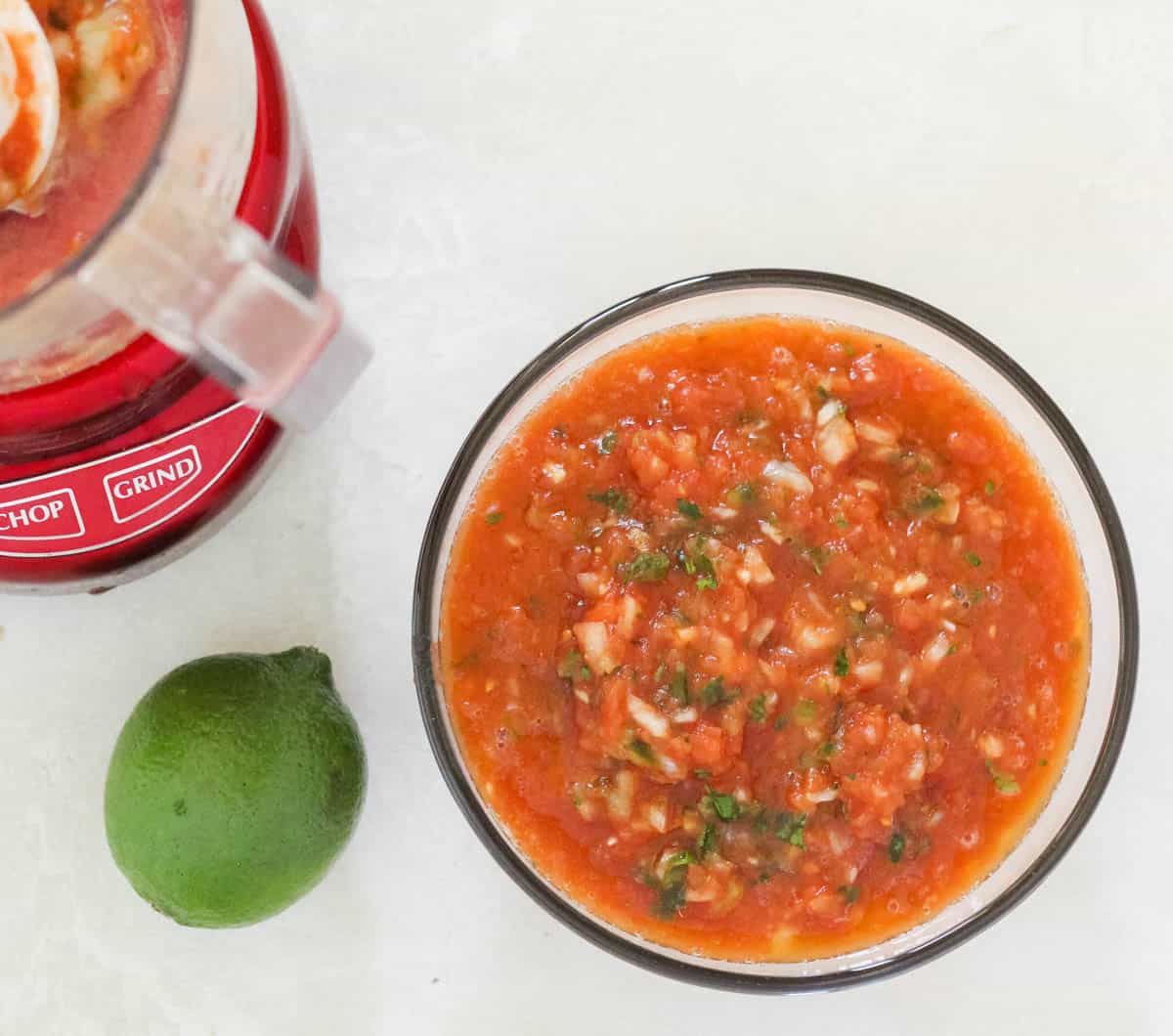 red mini food processor next to a fresh lime and a bowl of salsa.