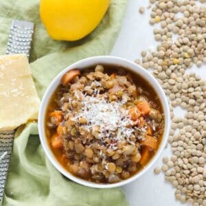 bowl of lentil soup topped with cheese next to scattered green lentils and a Microplane with parmesan cheese.