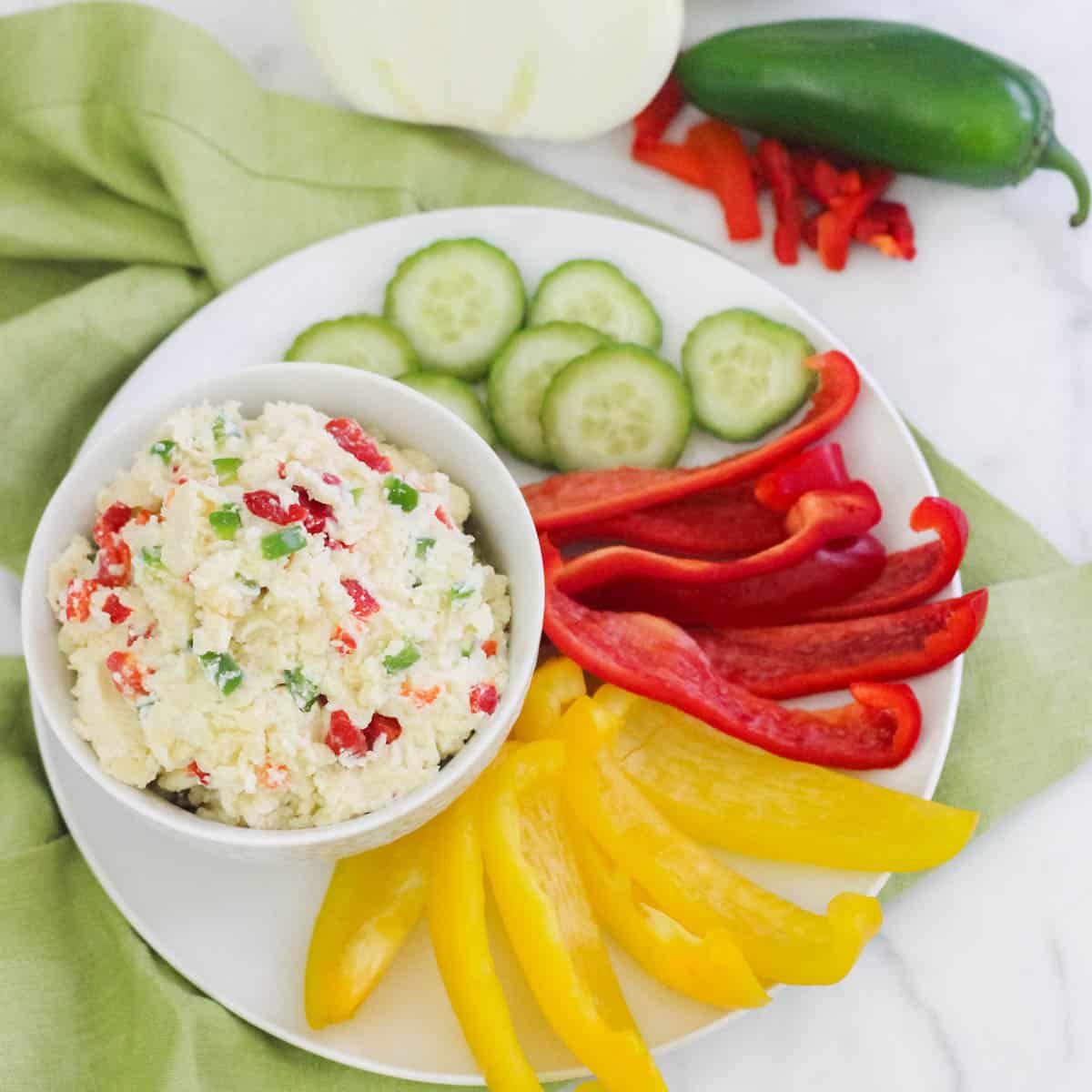 green napkin under a plate with sliced veggies and a bowl of pimento cheese with jalapenos.