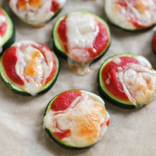 baked zucchini slices topped with pizza sauce and cheese on a parchment lined baking sheet.
