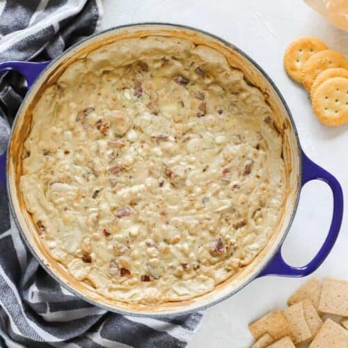 blue baking dish with hot blue cheese dip with bacon and walnuts surrounded by a towel and crackers.