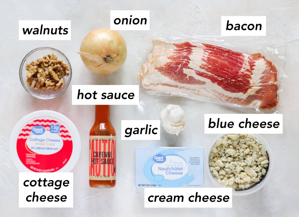 bowl of walnuts, container of cottage cheese, bottle of hot sauce, block of cream cheese, container of blue cheese, head of garlic, package of bacon, whole yellow onion with text overlay describing ingredients.
