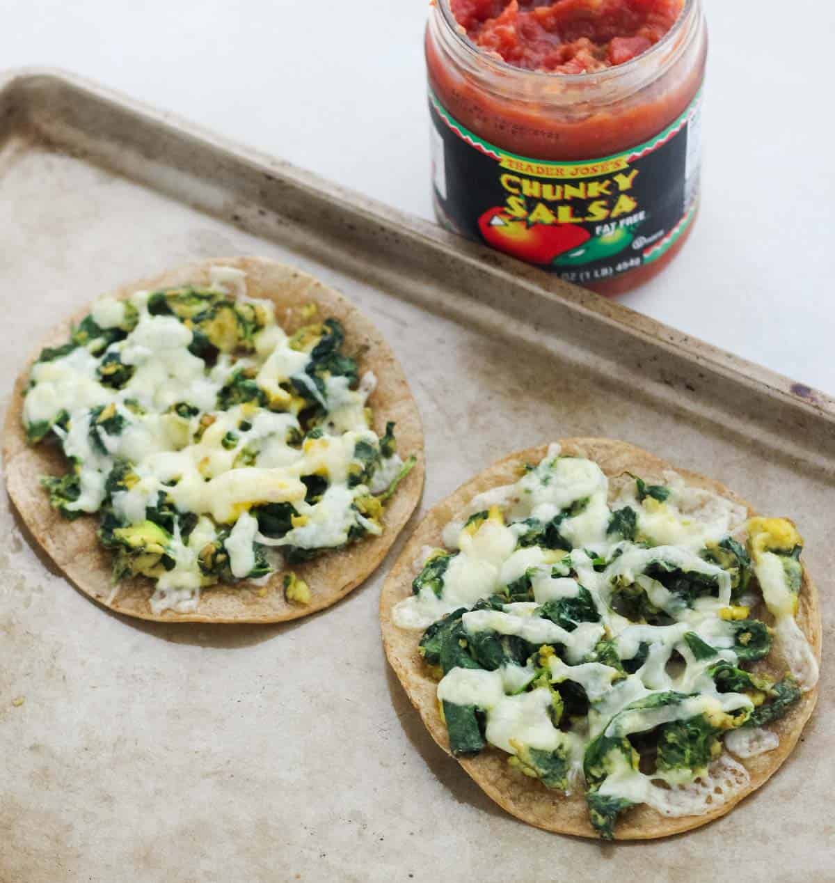 baking sheet with two scrambled egg breakfast tostadas with spinach next to a jar of salsa.