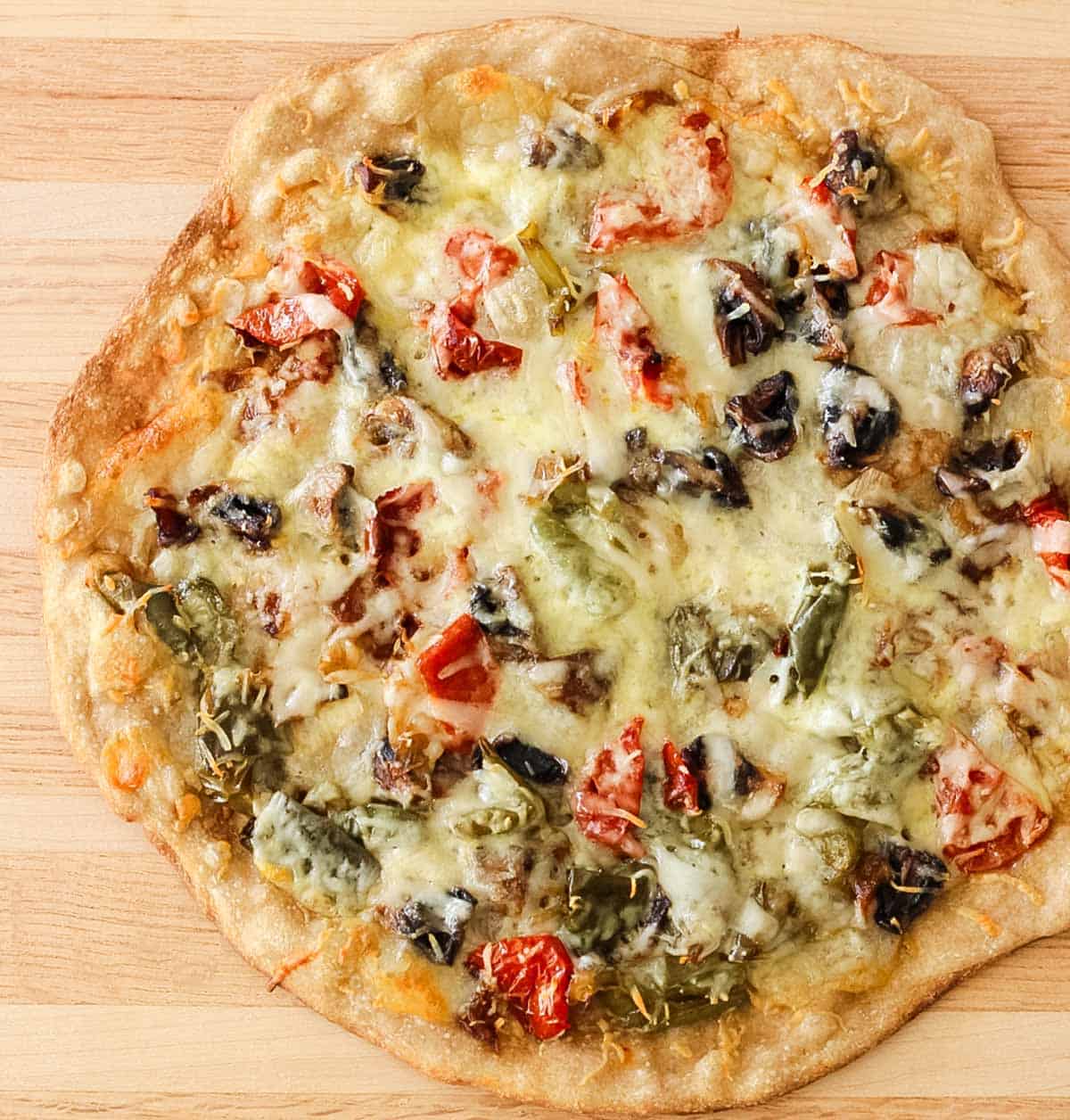 wooden cutting board with a baked roasted veggie white pizza before being cut.