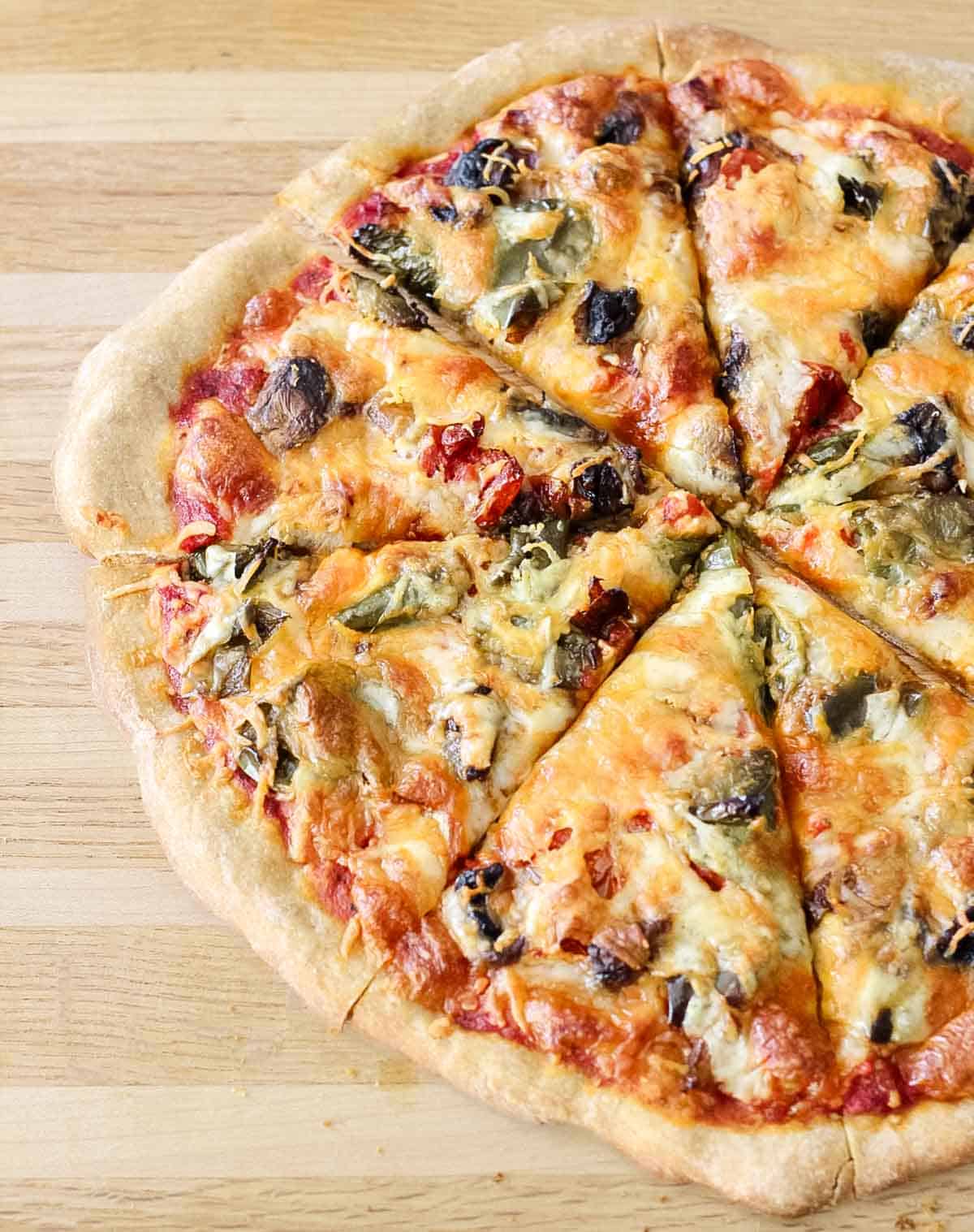 wooden cutting board with a baked and sliced roasted veggie pizza.