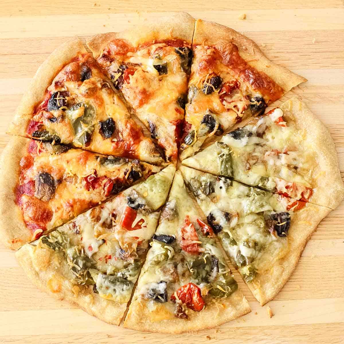 wooden cutting board with pizza slices from a roasted veggie pizza that has pizza sauce and half without pizza sauce.