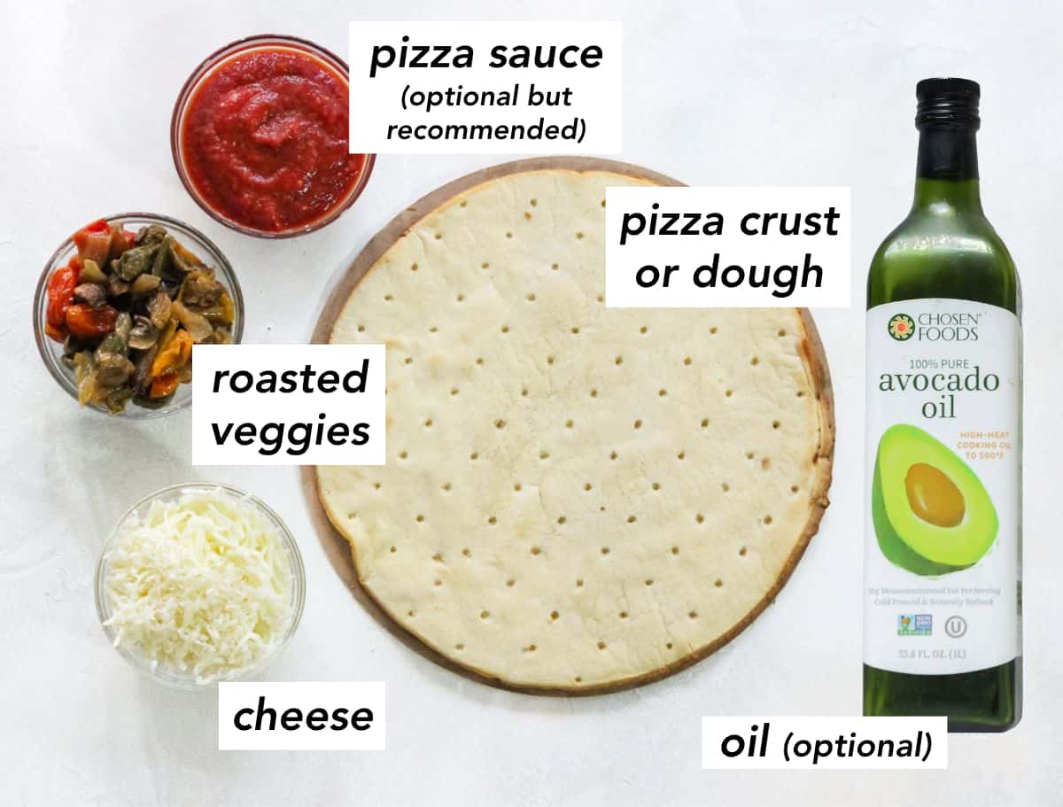 white counter with a bowl of pizza sauce, a bowl of roasted veggies, a bowl of shredded cheese, an unbaked pizza crust, and a bottle of avocado oil with text overlay describing ingredients.