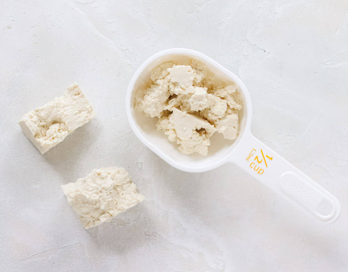 white half cup measuring cup with crumbled tofu.