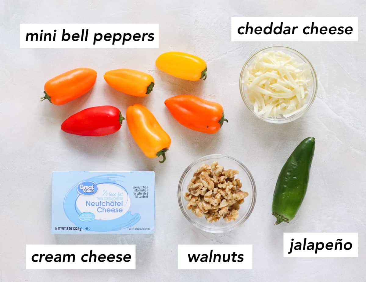 bowl of walnuts, jalapeno, bowl of shredded cheddar cheese, block of cream cheese, and baby bell peppers on white counter with text overlay describing ingredients.