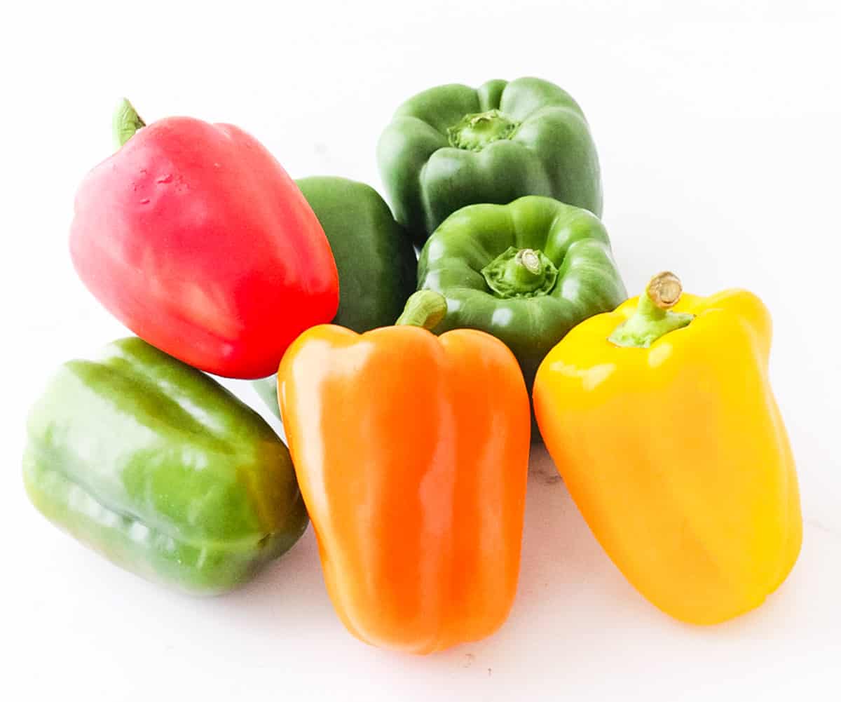 red, green, orange, and yellow bell peppers on a white counter.