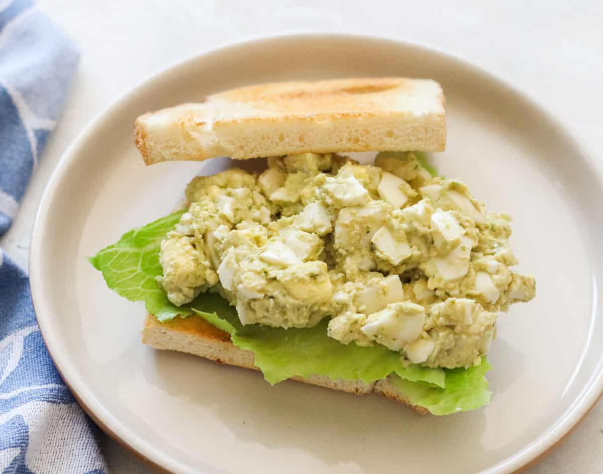 hummus egg sandwich on a plate with lettuce next to a blue napkin.