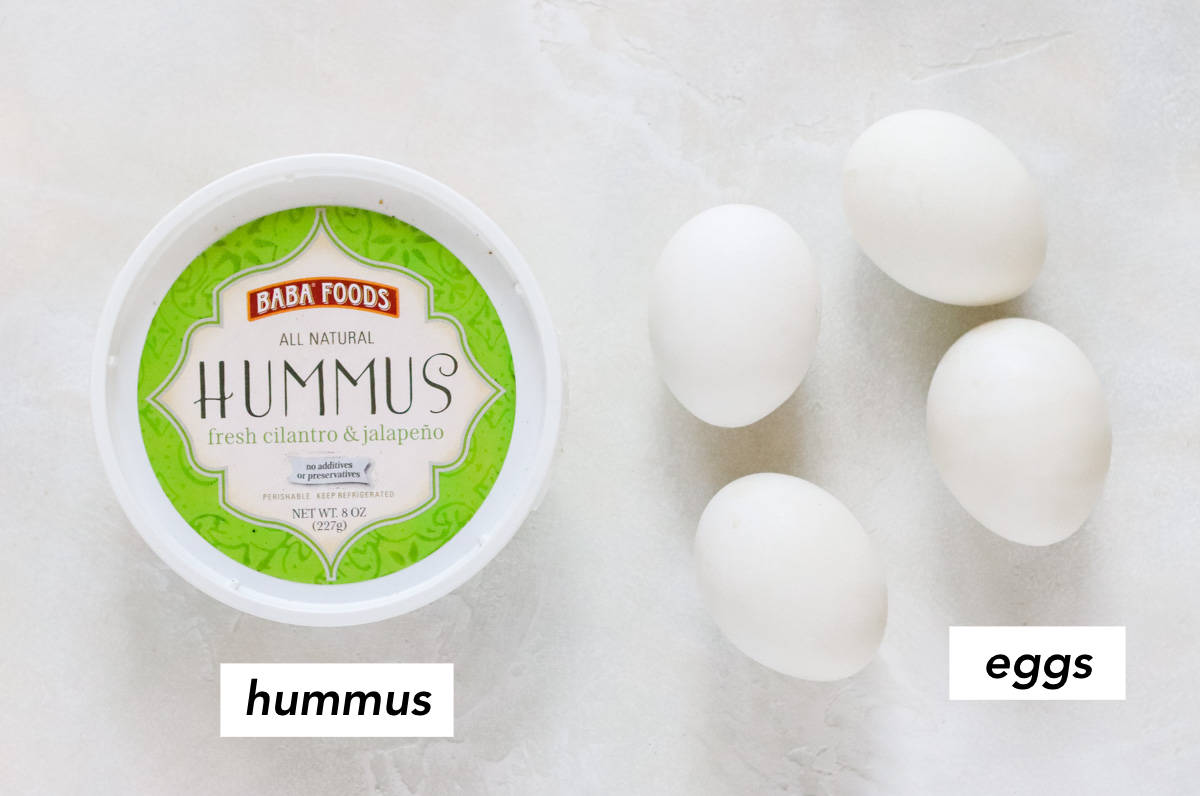 container of hummus and four hard-boiled eggs on a white counter.