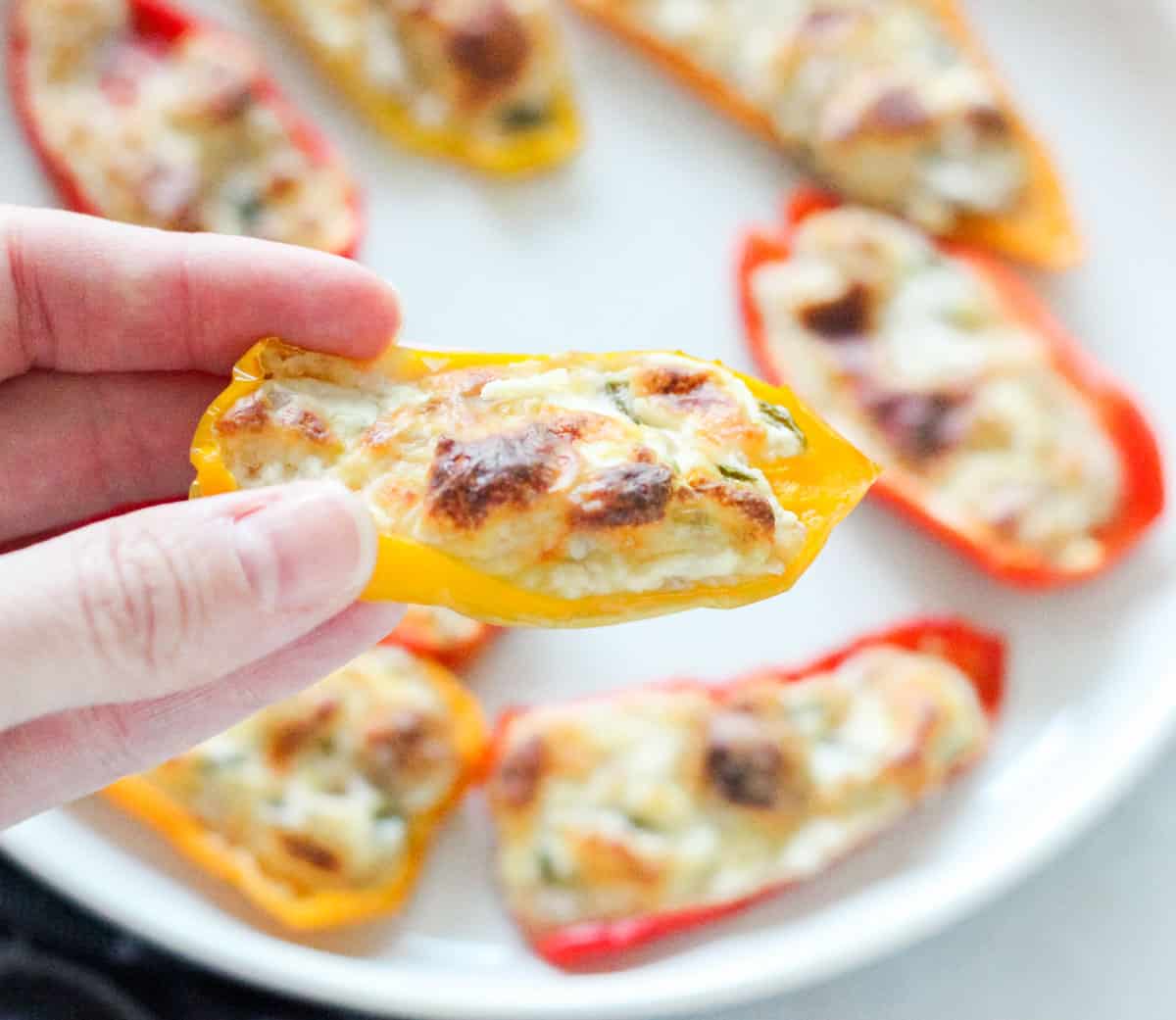 hand holding a mini bell pepper stuffed with cream cheese and a plate of cold cream cheese stuffed baby bell peppers.