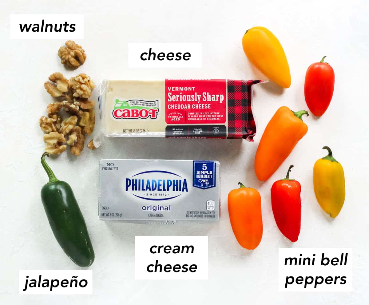 walnuts, jalapeno, block of cheddar cheese, block of cream cheese, and orange, yellow, and red baby bell peppers on white counter with text overlay describing ingredients.