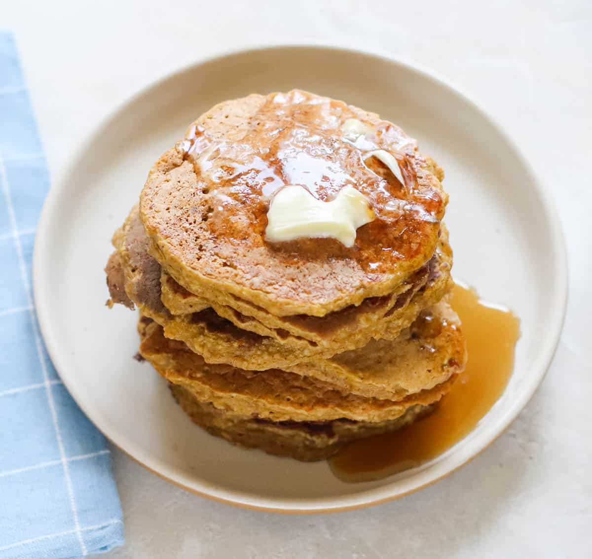 plate of pumpkin pancakes covered in butter and syrup next to a baby blue and white napkin.