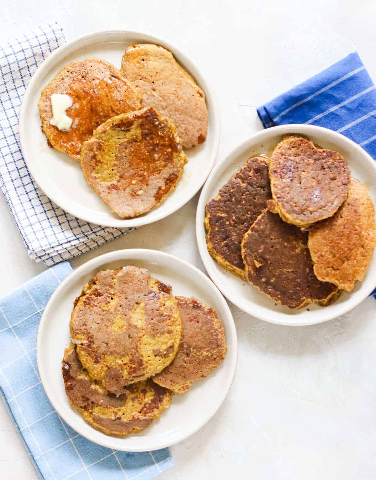 three plates with pumpkin pancakes next to an array of blue and white napkins.