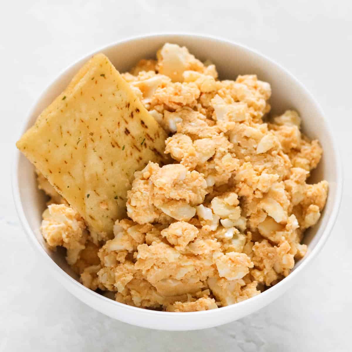 pita chip in a bowl of hummus egg salad using red pepper hummus.