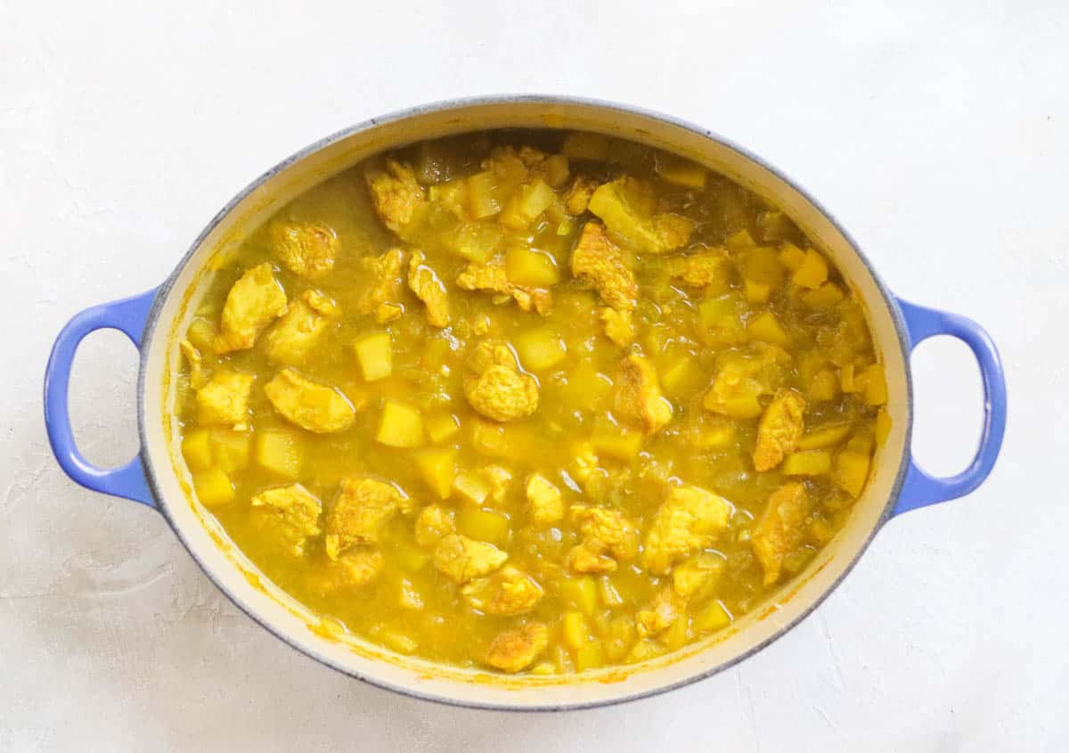 blue pot with apple chicken curry sauce on a white counter.