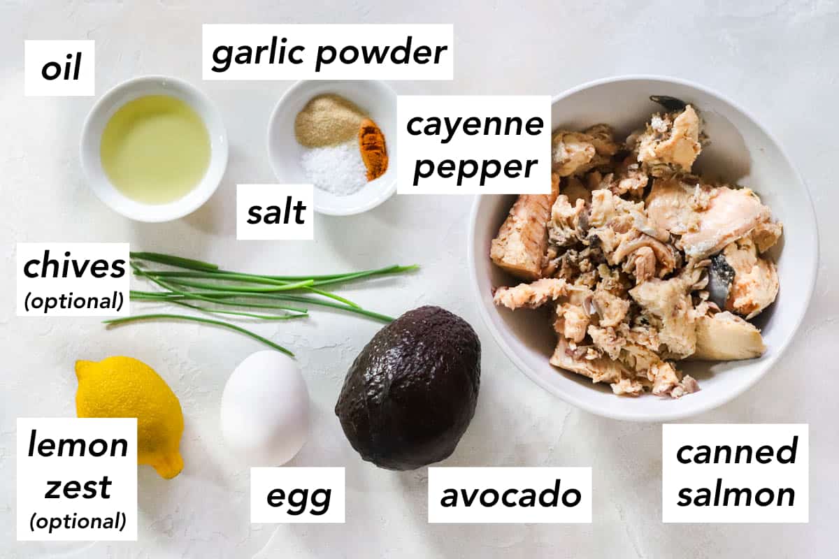 ingredient photo with text labeling item: oil, garlic powder, cayenne pepper, salt, canned salmon in a white bowl, avocado, egg, lemon, chives.