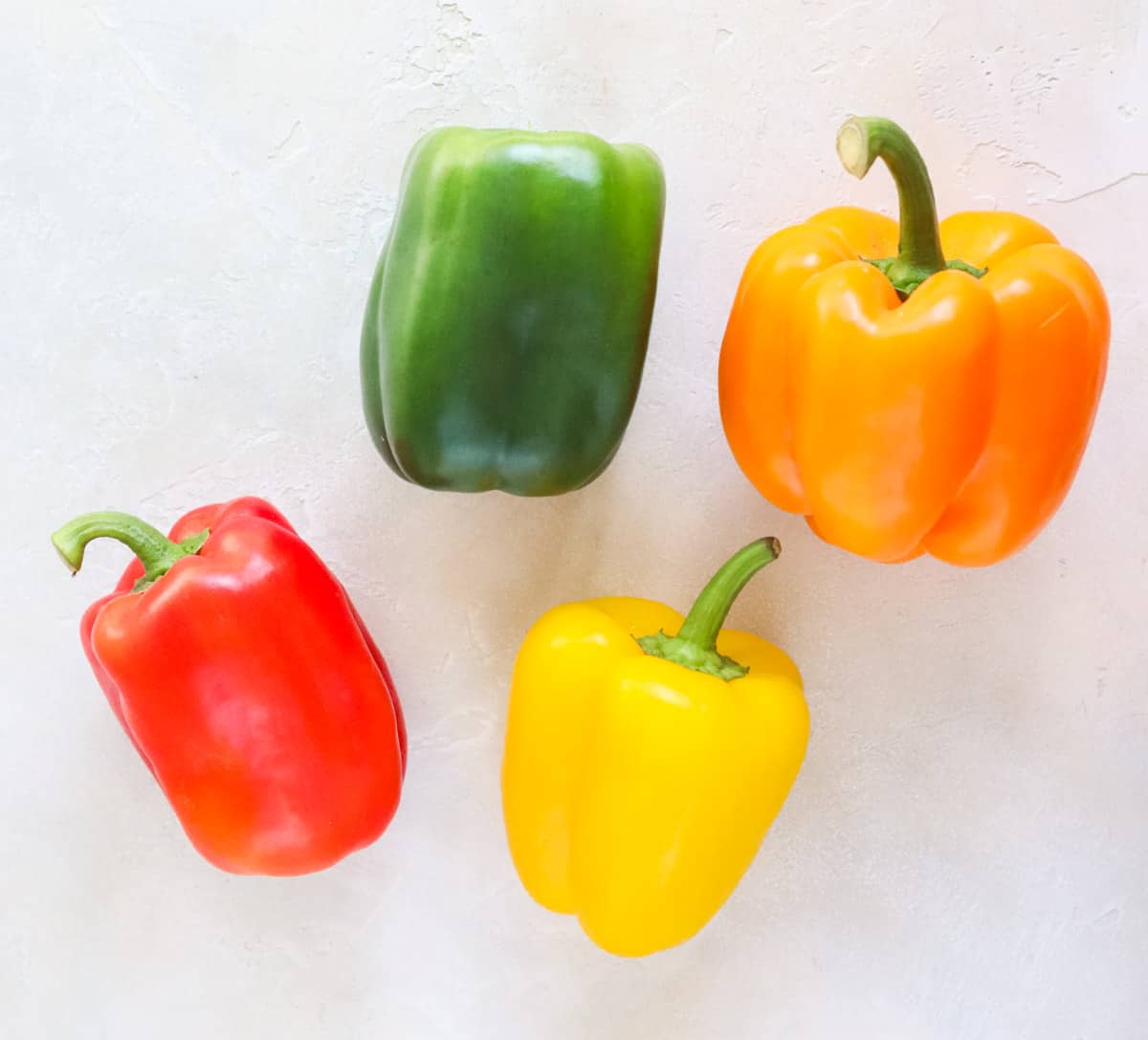 fresh red, yellow, orange, and green bell peppers on a white counter.
