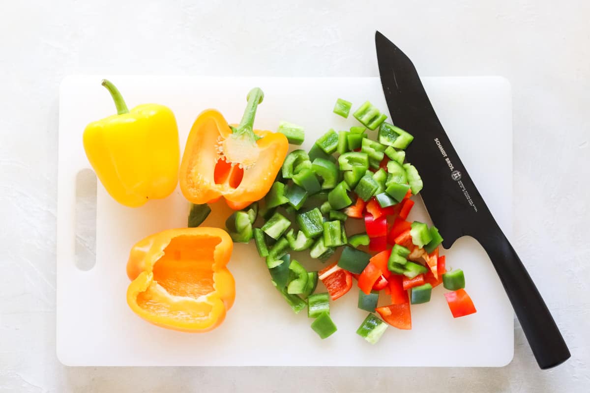 plastic cutting board with chopped green, red, yellow, and orange bell peppers with black knife.