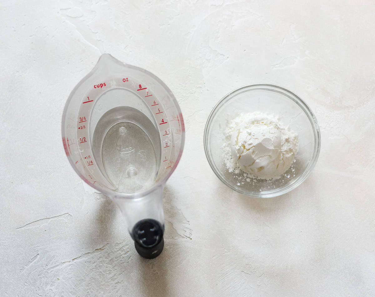 measuring cup with water next to a small bowl of cornstarch.
