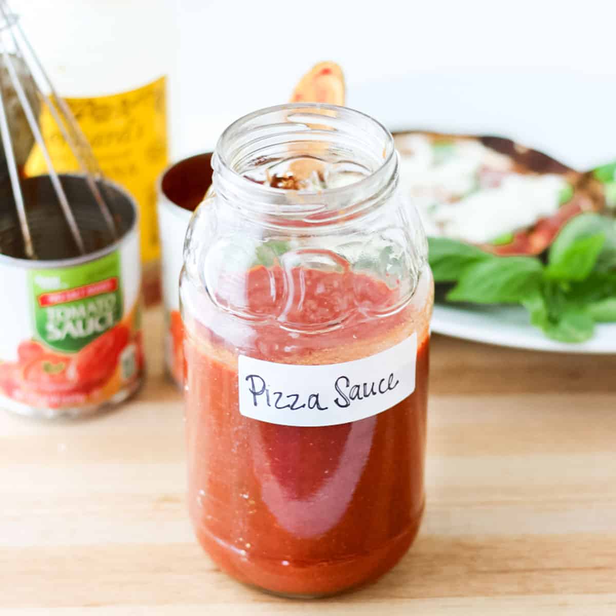 jar of low salt pizza sauce with a handwritten label next to a can of tomato sauce and pita pizzas.