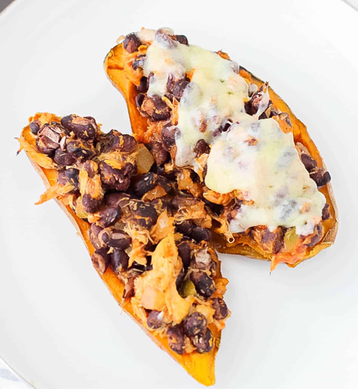 white plate with two black bean, chicken, and cheese topped stuffed sweet potatoes.