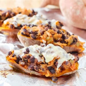 4 stuffed sweet potato topped with chicken, black beans, and cheese on foil-lined baking sheet.