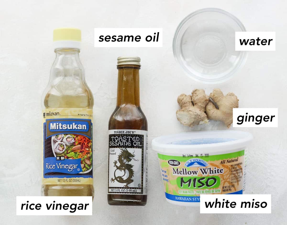 rice vinegar, toasted sesame oil, small bowl of water, fresh ginger root, and white miso container on white counter.