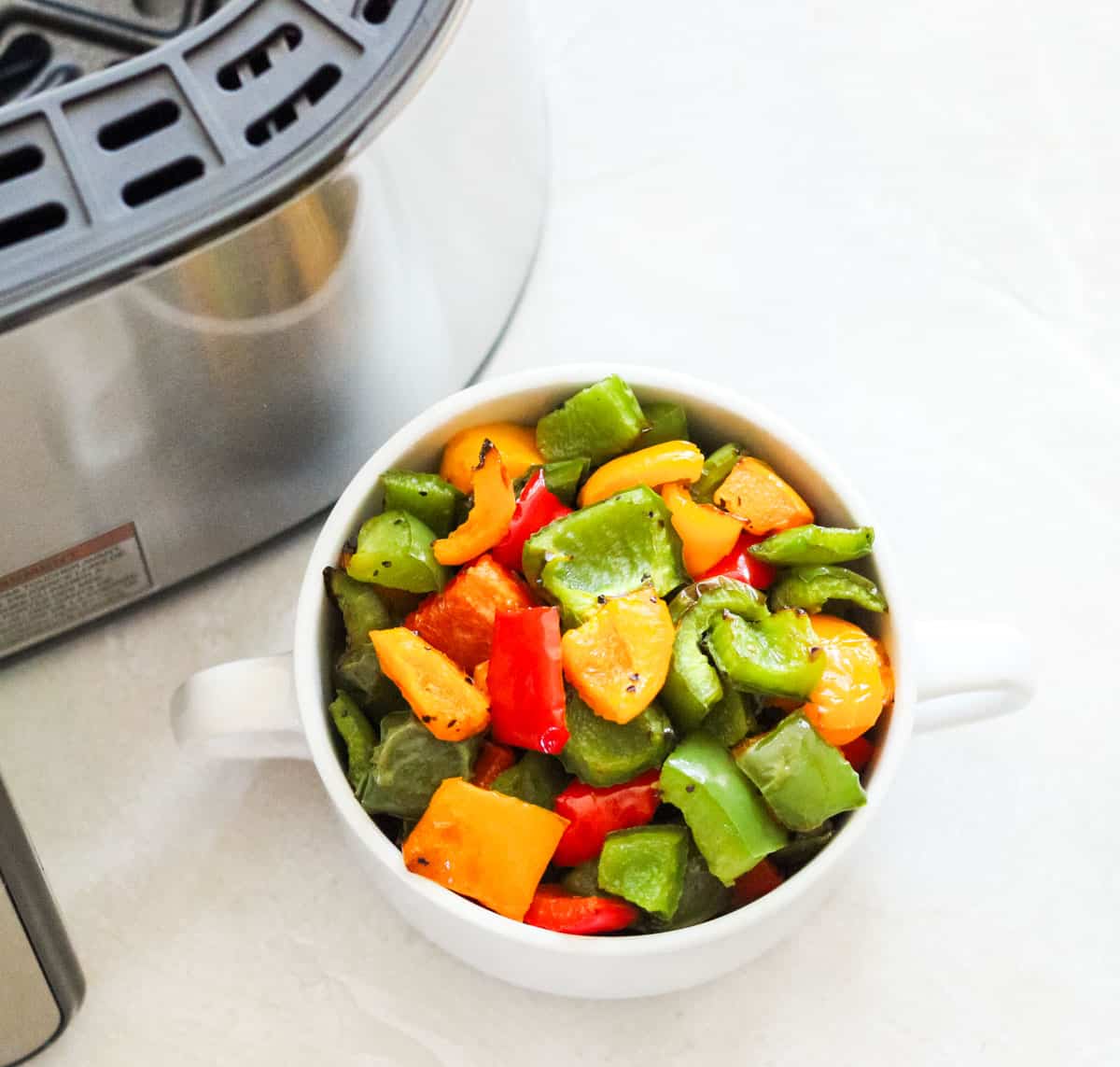white bowl of roasted bell peppers next to an air fryer.