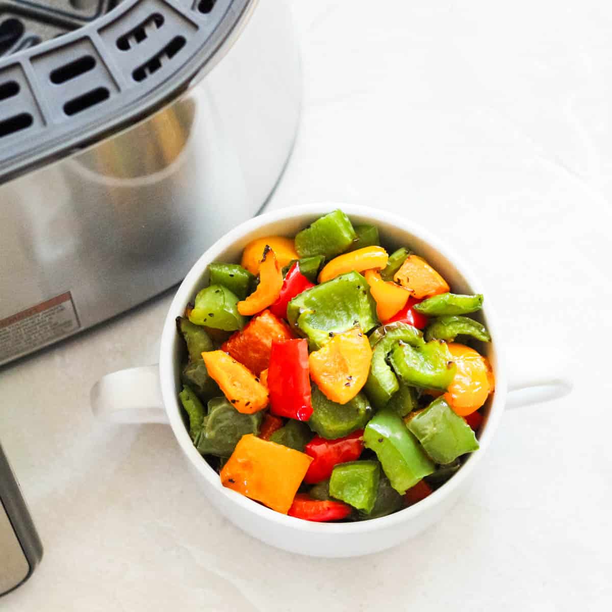 white bowl of roasted bell peppers next to a silver air fryer.
